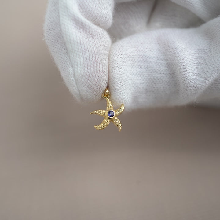 Starfish pendant in gold and with gemstone Iolite, the birthstone of September. Birthstone charm with Iolite crystal in a golden starfish.